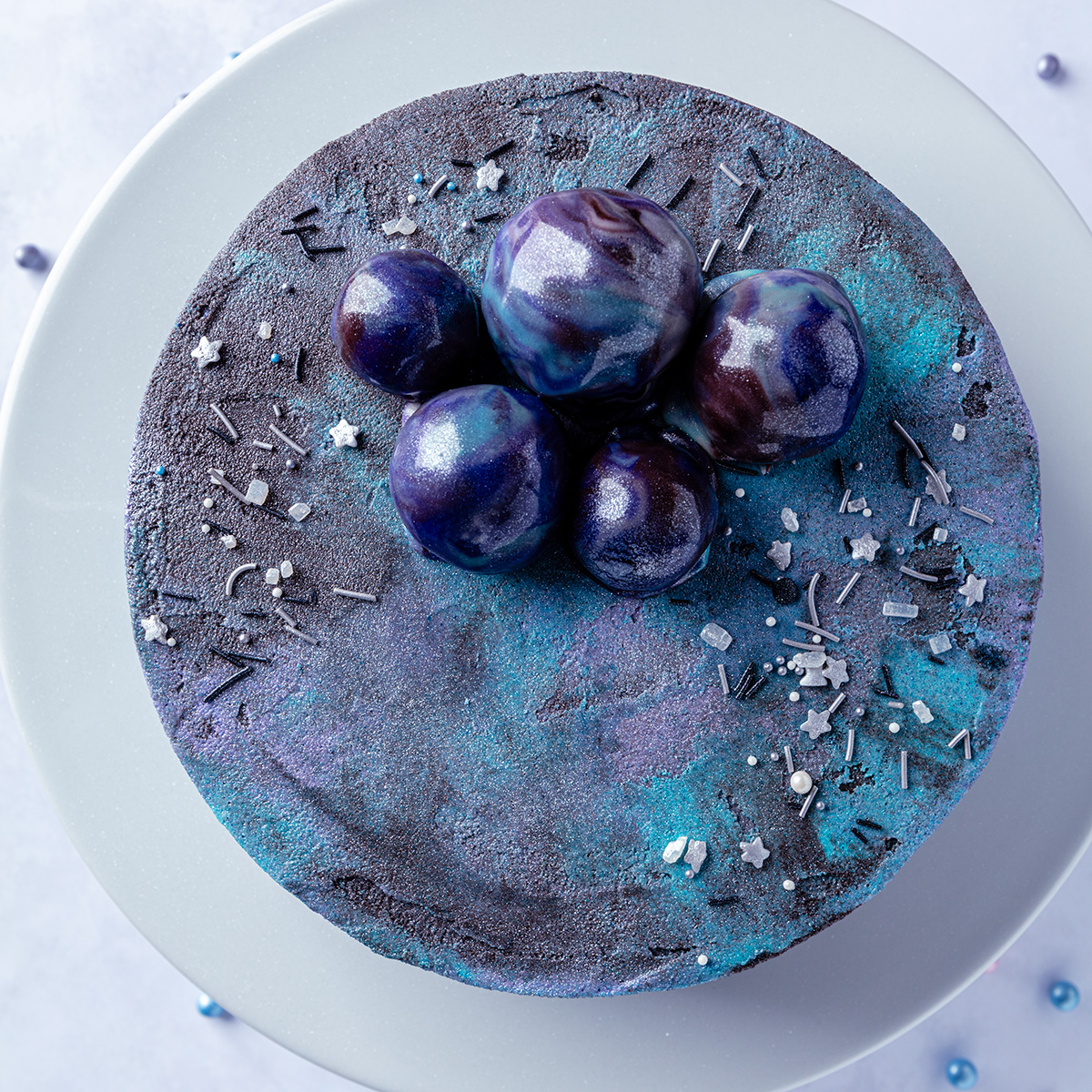 a galaxy cake with asteroids on top of the cake and moons and stars sprinkles.