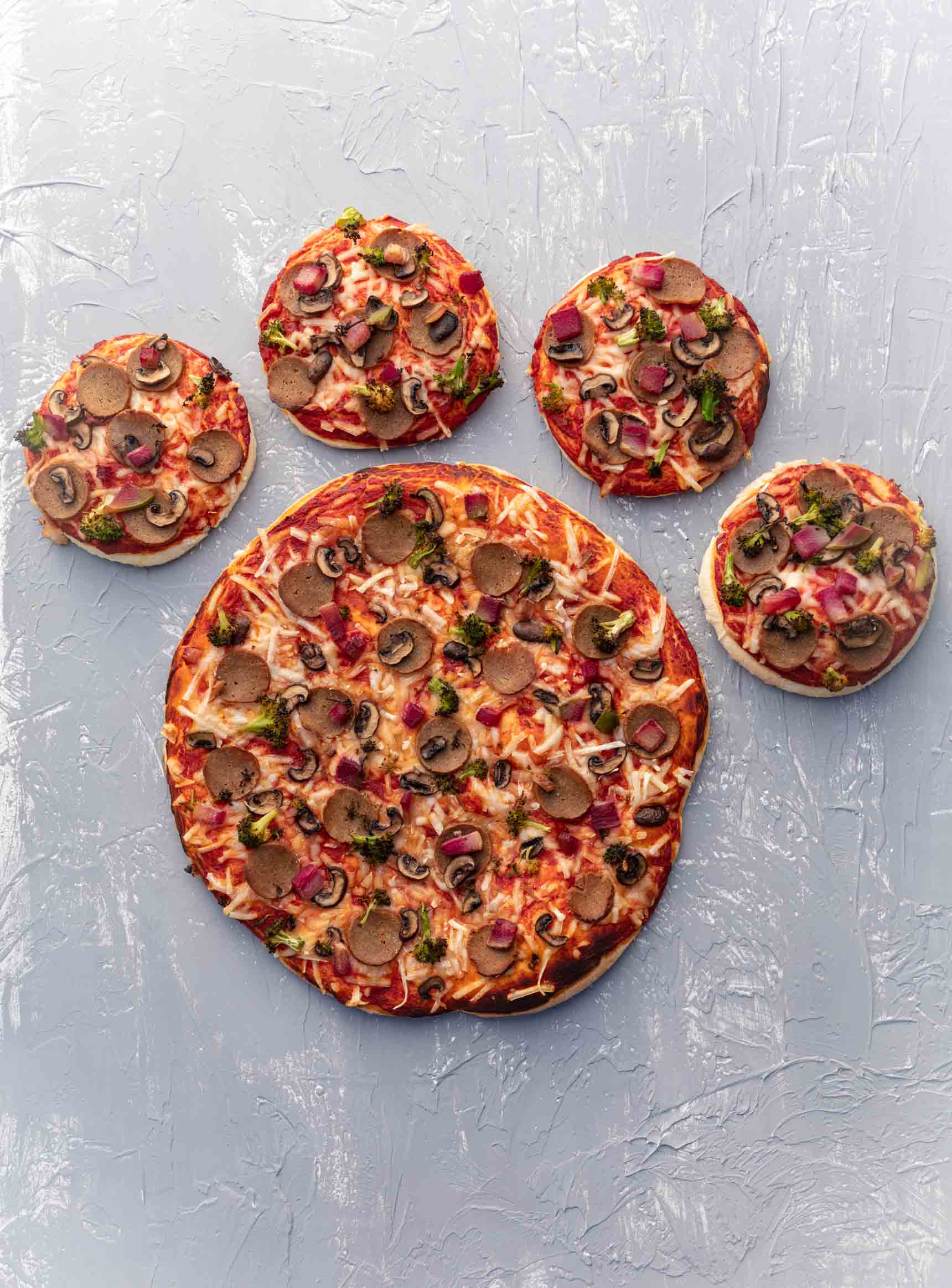 4 vegan pizzas arranged in the shape of a large paw print