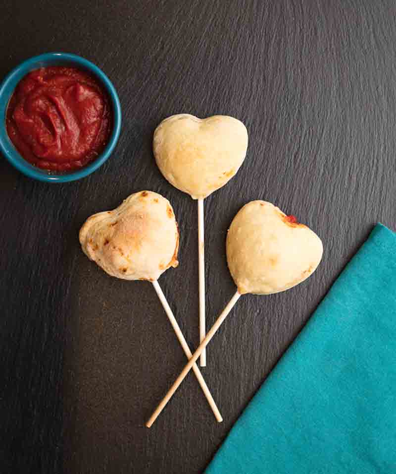 3 pepperoni pizza heart shaped lollipops on a slate.