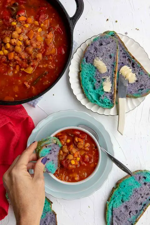 dipping unicorn colored bread into a bowl of 10 vegetable soup