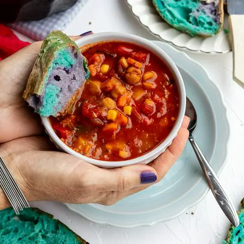 Robin holding a bowl of Panera’s 10 vegetable soup with a piece of colorful bread in it