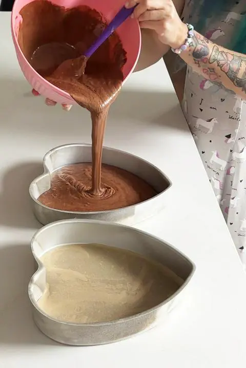 Pouring vegan chocolate cake batter into heart cake pans.