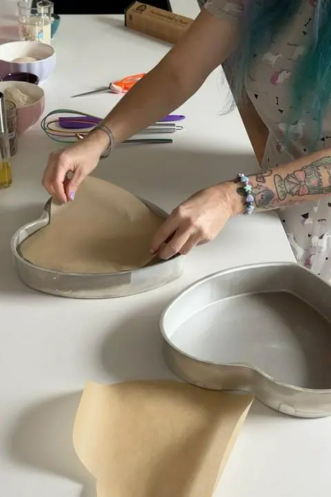 Prepping the heart cake pans with parchment paper.