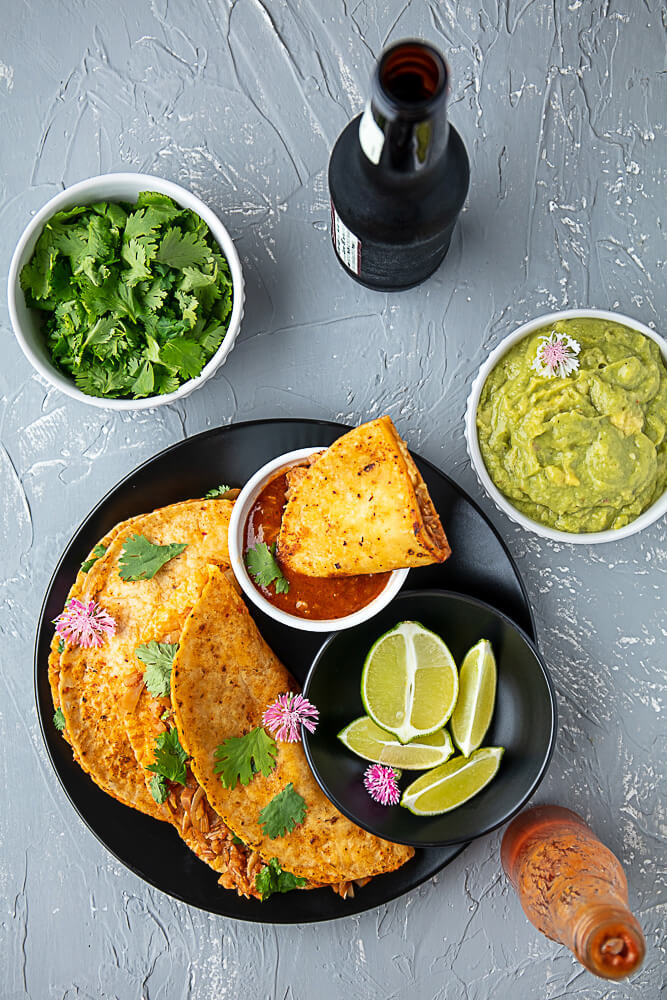 2 vegan quesabirria tacos on a plate, and another being dipped in a small bowl of consommé