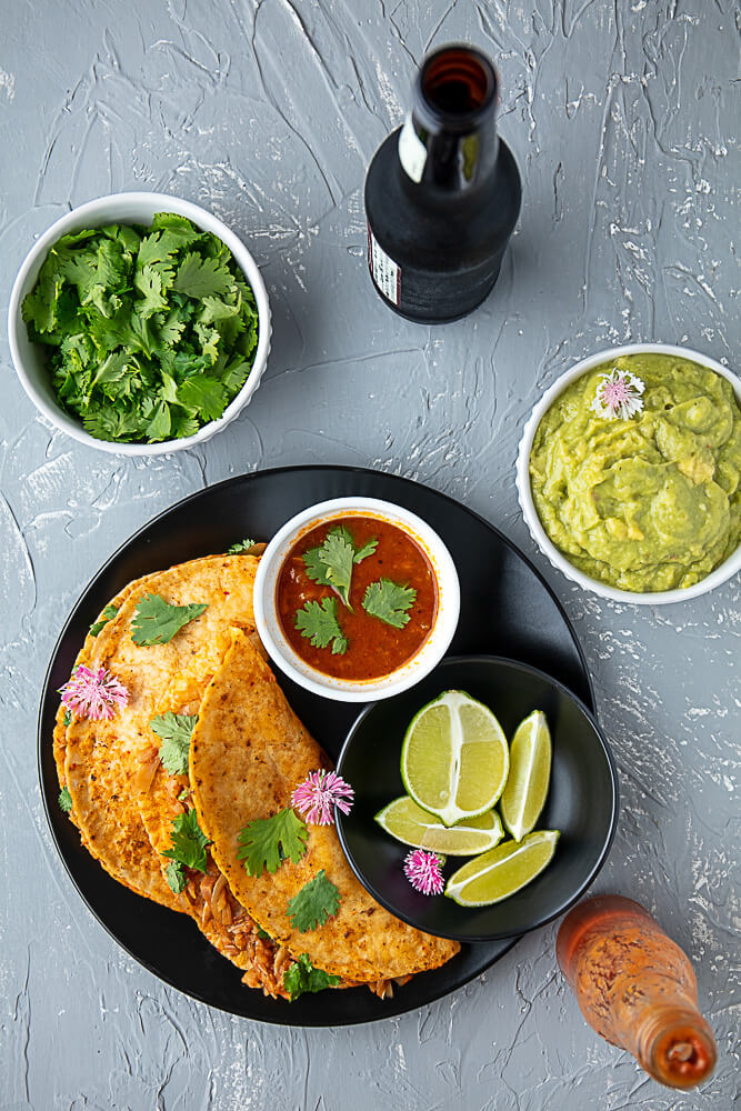 2 vegan quesabirria tacos on a plate, garnished with cilantro and pink edible flowers