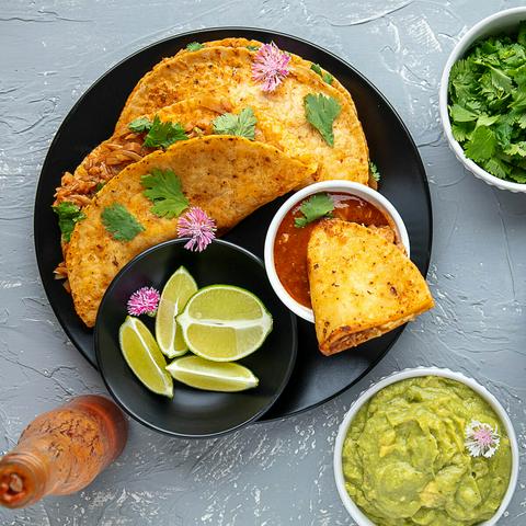 2 vegan quesabirria tacos on a plate, garnished with cilantro and pink edible flowers