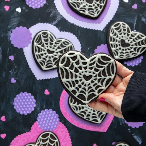 holding a vegan black heart cookie with other cookies in the background