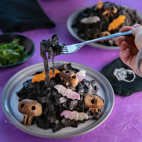 taking a bite of black halloween pasta with veggie bats and skull mushrooms