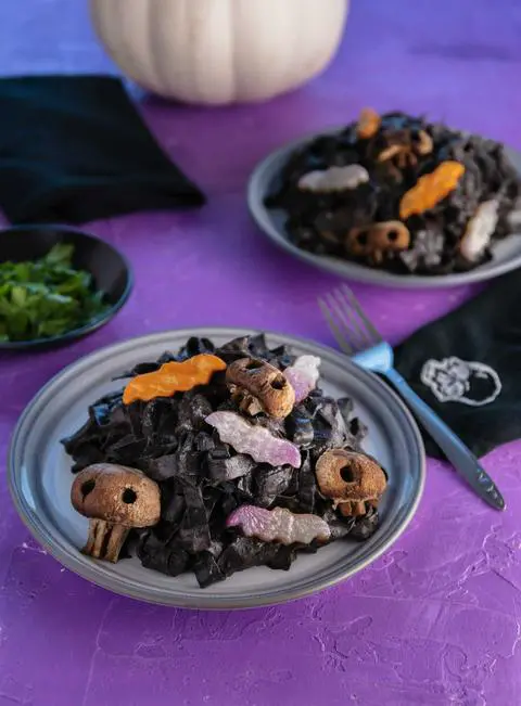 a plate of black bean pasta with bat veggies and skull mushrooms