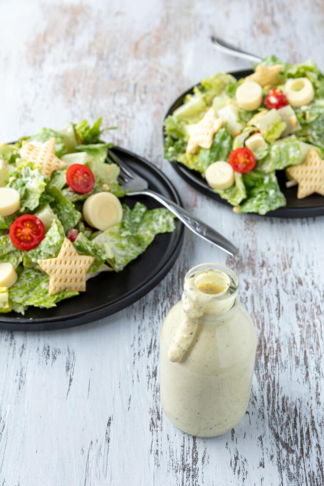 small bottle of caesar dressing with caesar salads in the background