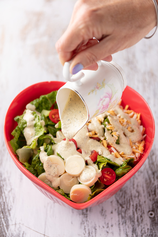 pouring the vegan caesar dressing onto a caesar salad