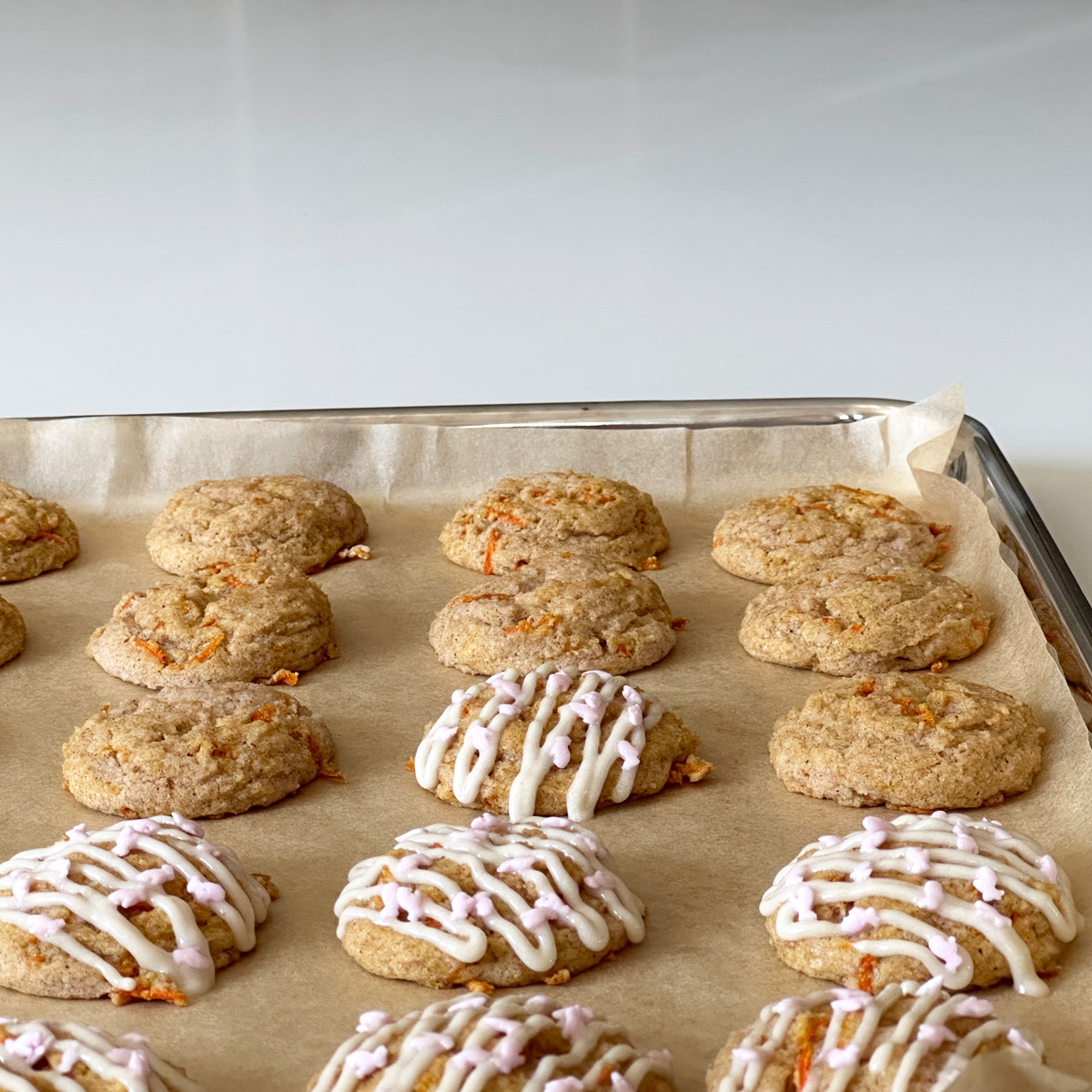 a tray of carrot cake cookies with a few of them iced and with light pink bunny sprinkles.