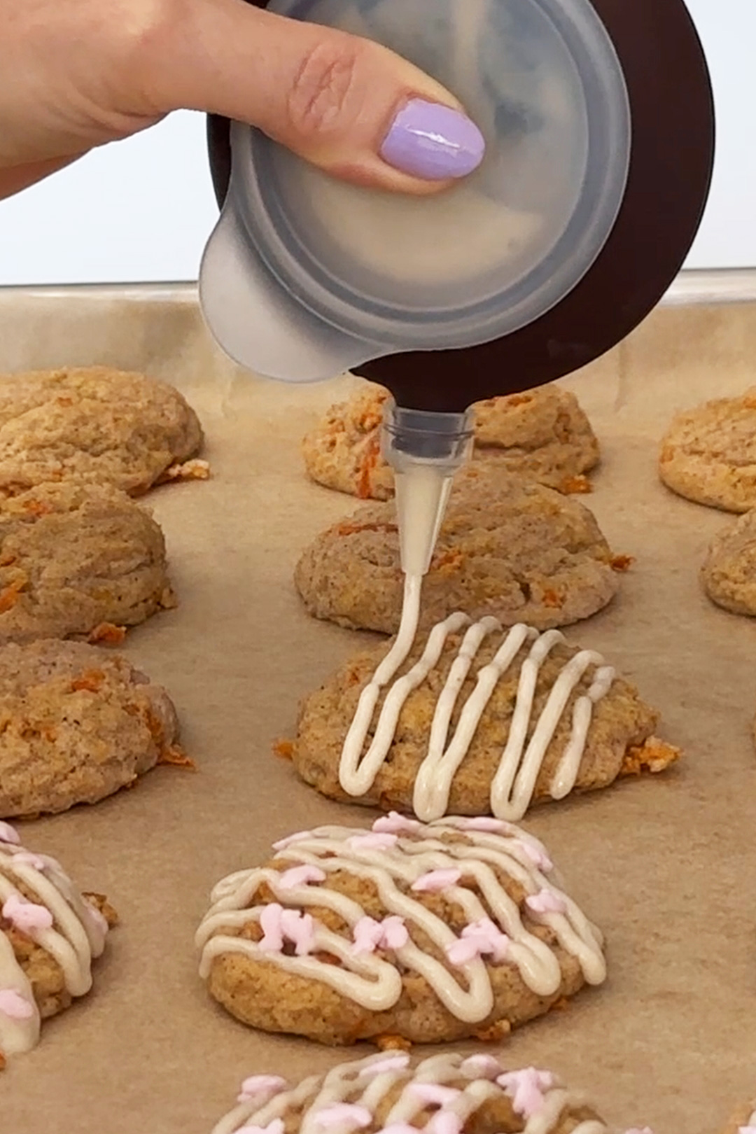 drizzling vegan cream cheese icing onto carrot cake cookies using a decopen.