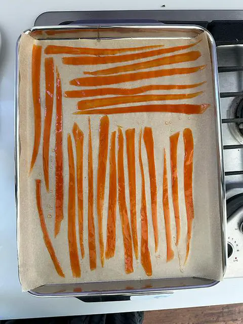 candied carrots lined up on a parchment paper lined baking sheet.