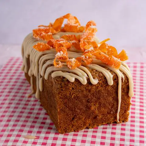 vegan carrot cake loaf with cream cheese icing and candied carrot twists on top.