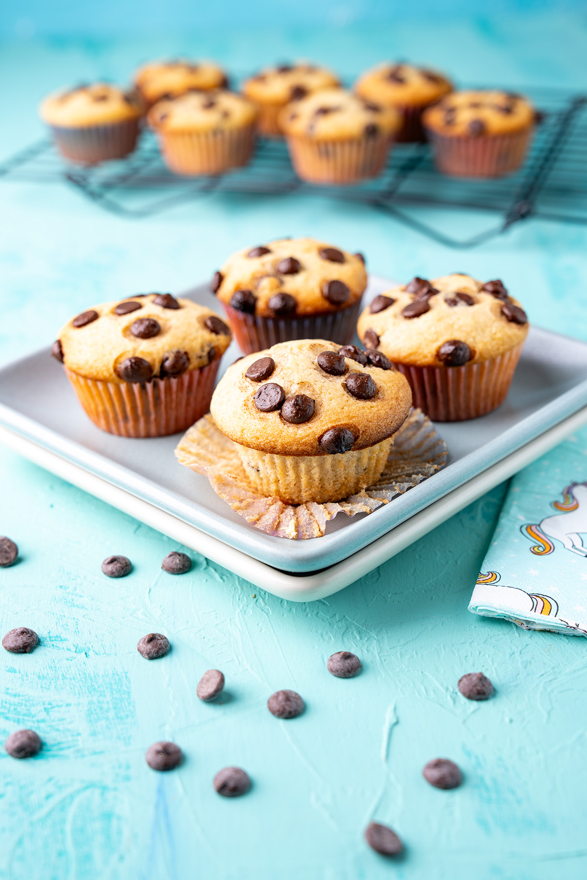 4 chocolate chip muffins made without eggs on a heath ceramics plate with the rest on the cooling rack in the background.