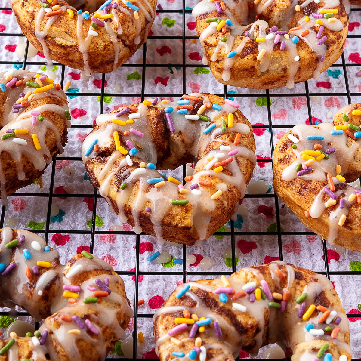 vegan cinnamon roll donuts topped with icing and Color Kitchen rainbow sprinkles
