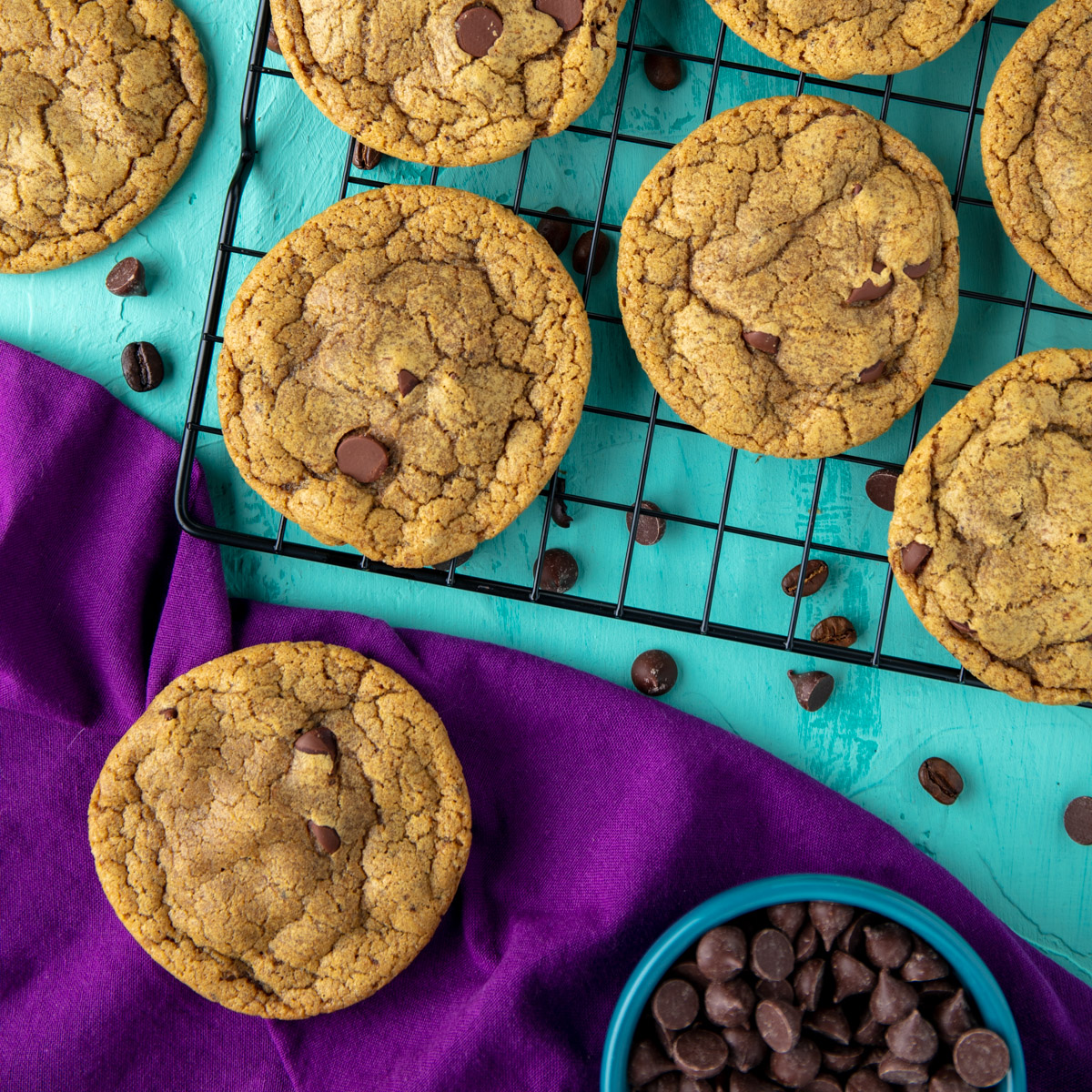 coffee chocolate chip cookies on a cooling rack with one on a purple napkin