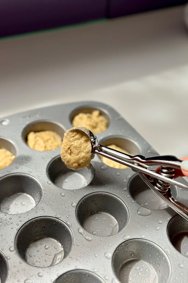 scooping vegan corn dog batter into a mini muffin pan