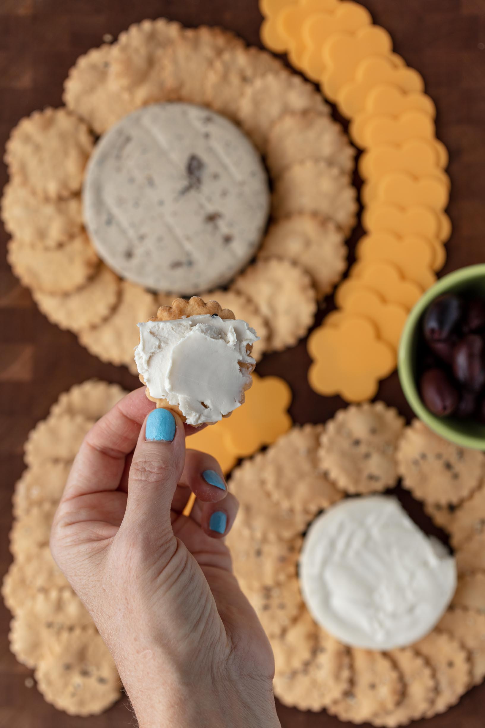 Closeup of a cracker with cheese on it, with the cheese and cracker charcuterie board in the background