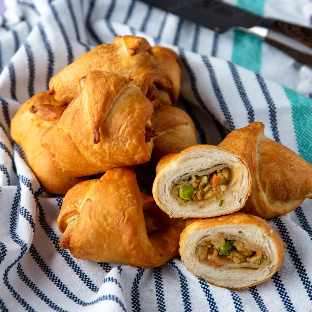 Golden crescent-roll triangles filled with spiced potato and peas, one cut open to show the filling.