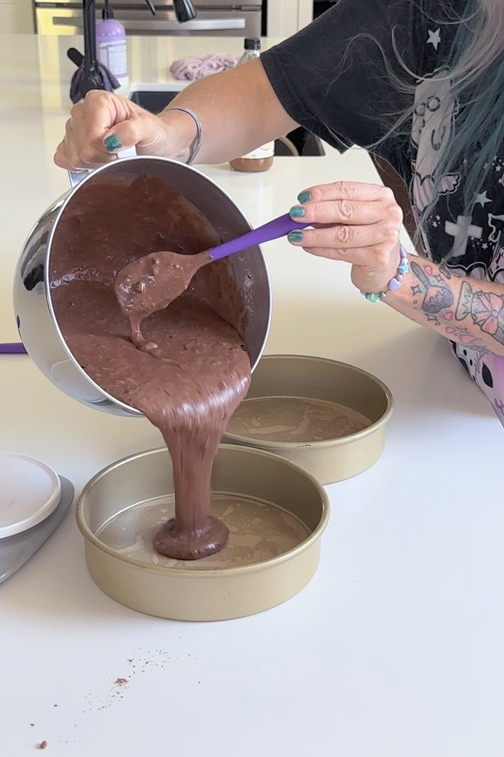 pouring vegan chocolate cake batter into round cake pans