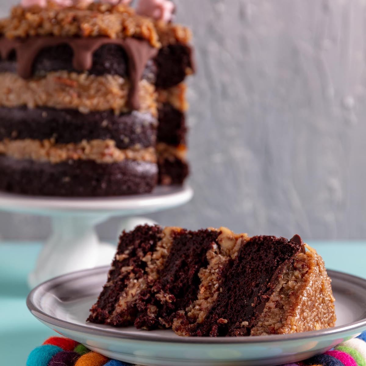 slice of vegan german chocolate cake with the rest of the cake in the background