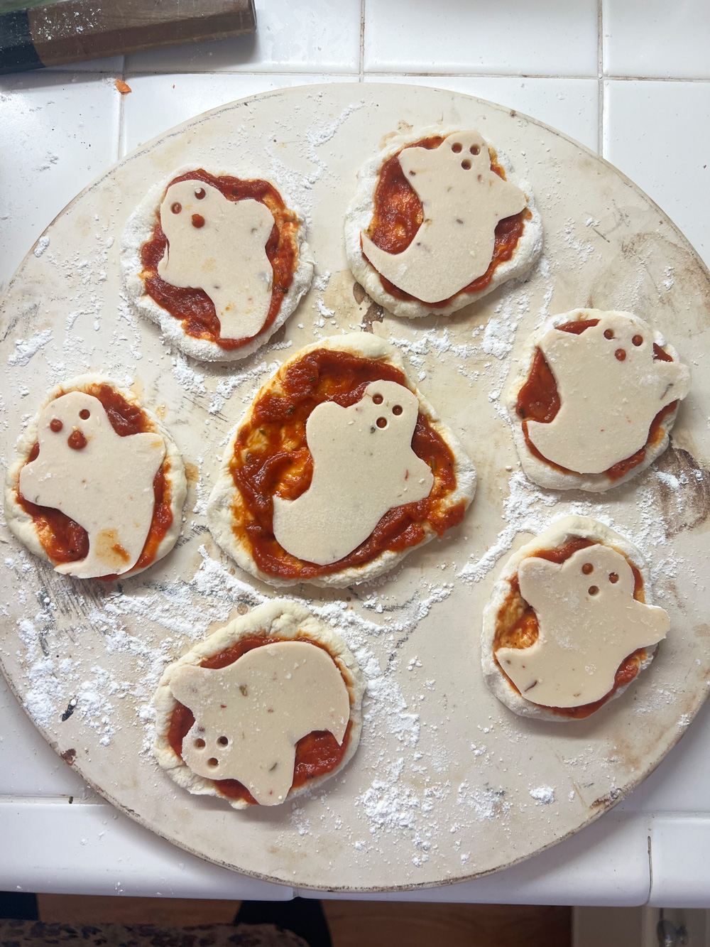 mini ghost pizzas on a baking stone