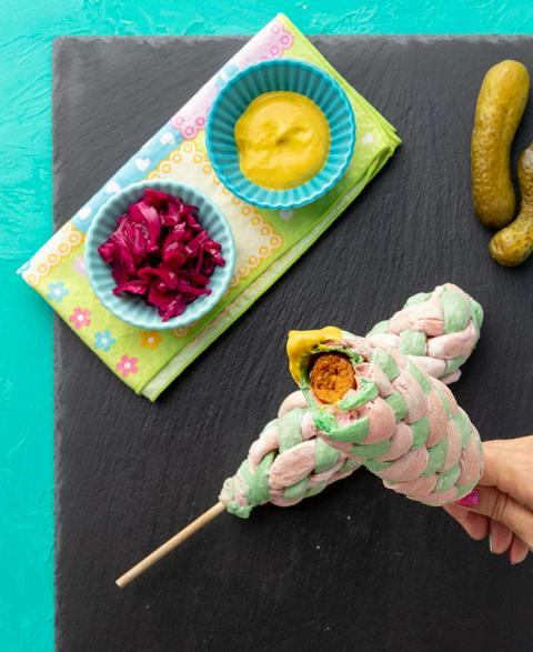 vegan hot dog on a stick wrapped in basket-weaved garlic knot dough with a bite missing