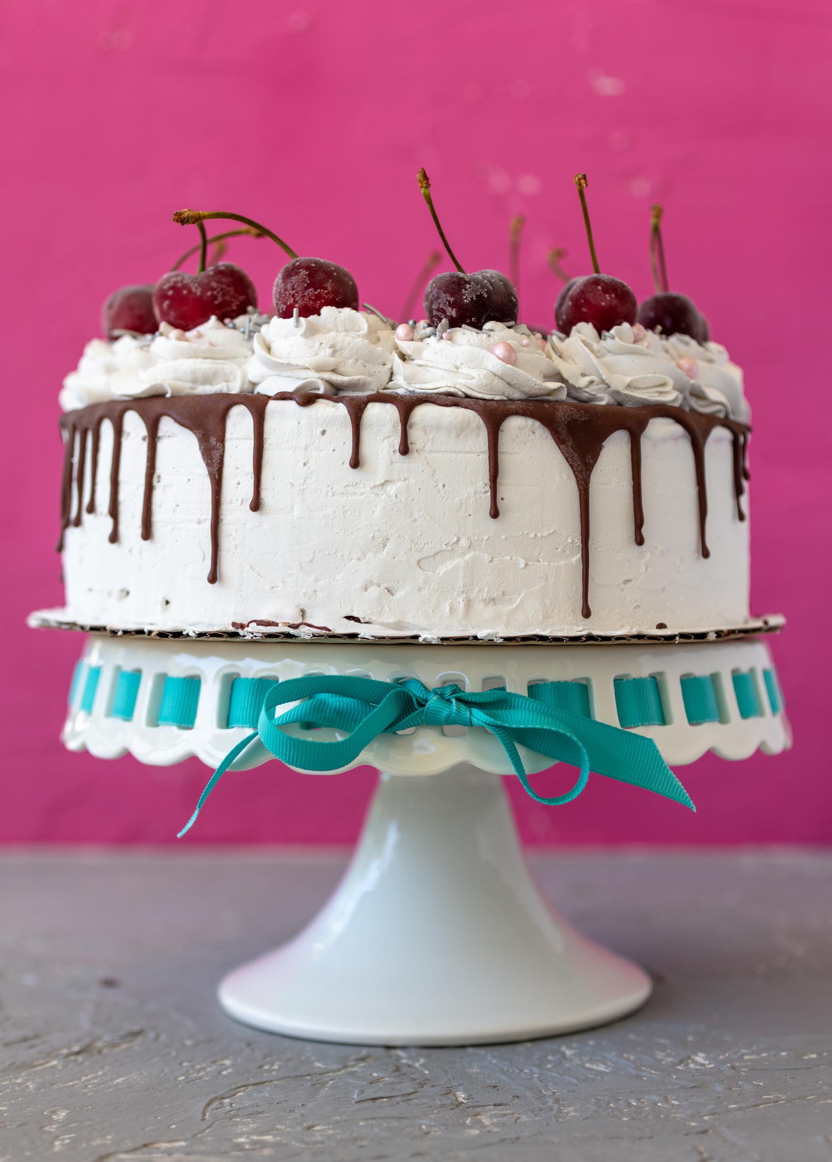 vegan ice cream cake with chocolate drips down the sides and frosty cherries on top