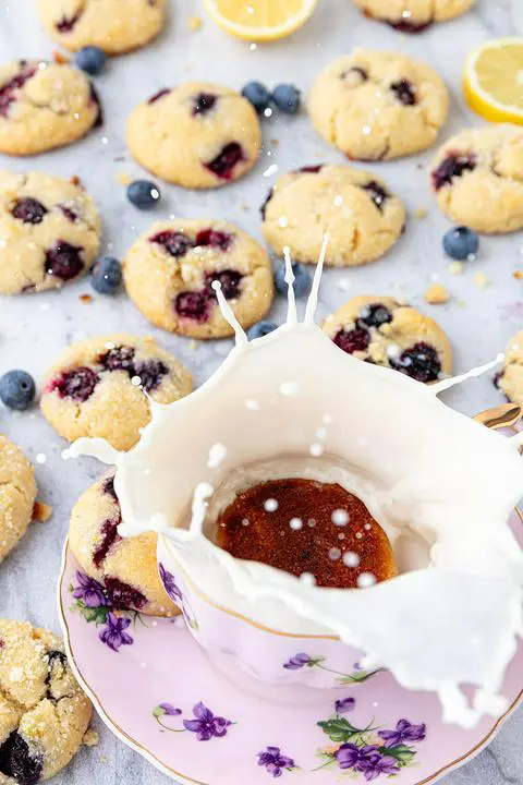 a lemon blueberry cookie falling into a glass of dairy-free milk