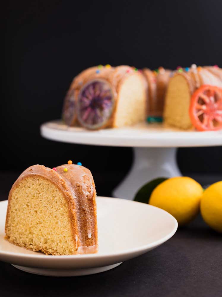 slice of vegan lemon bundt cake with the rest of the cake blurred in the background