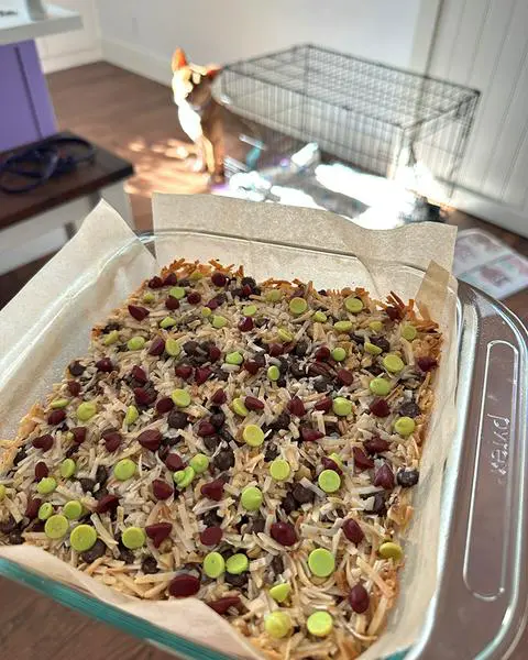 a square pan of magic bars cooled and ready for the fridge with a dog in the background.