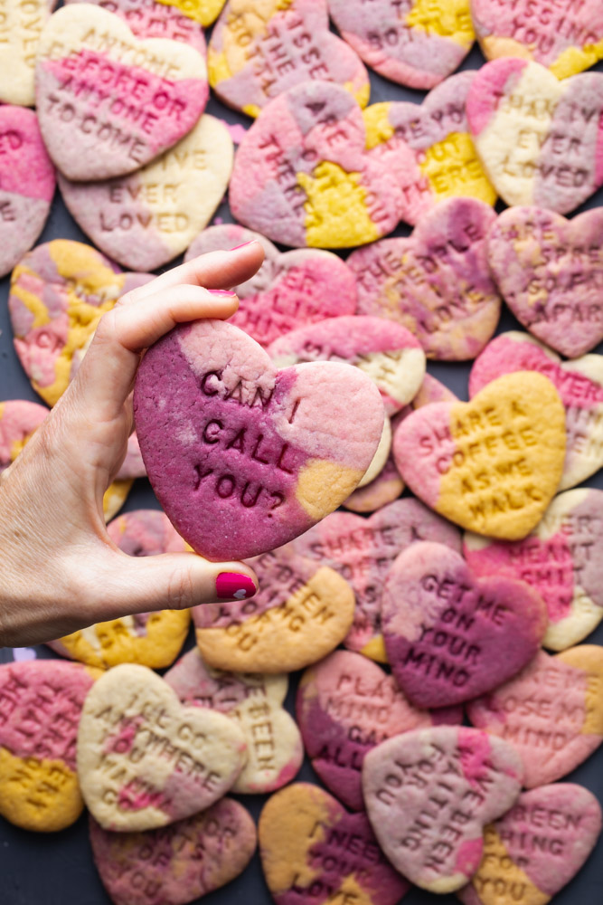 holding a marble colored vegan conversation heart cookie over a whole bunch of cookies