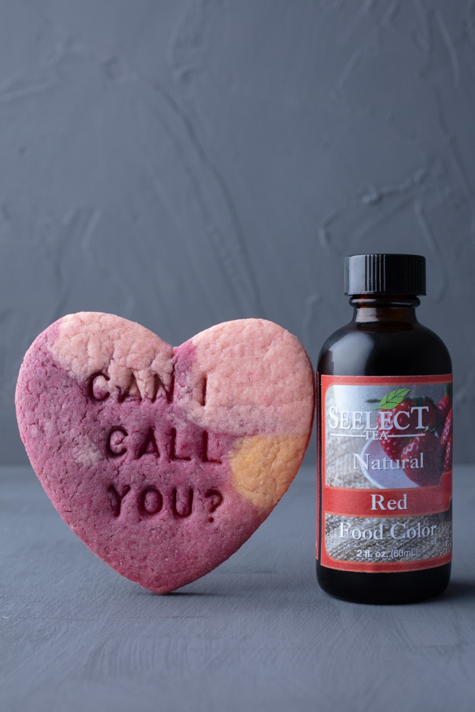 a vegan conversation heart sugar cookie leaning against a bottle of Nature’s Flavors food coloring