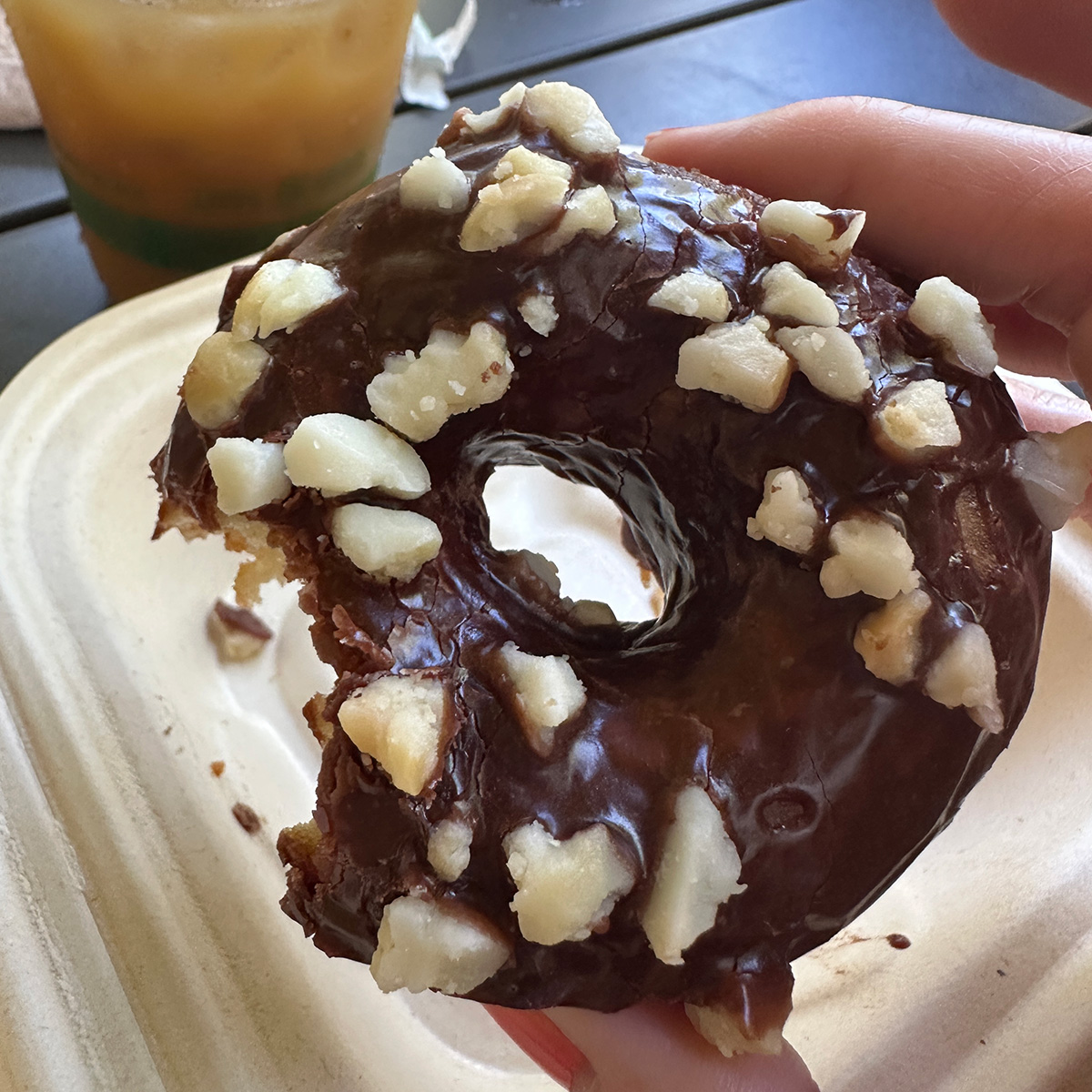 a vegan donut with chocolate glaze and pieces of macadamia nut on top has a bite missing.