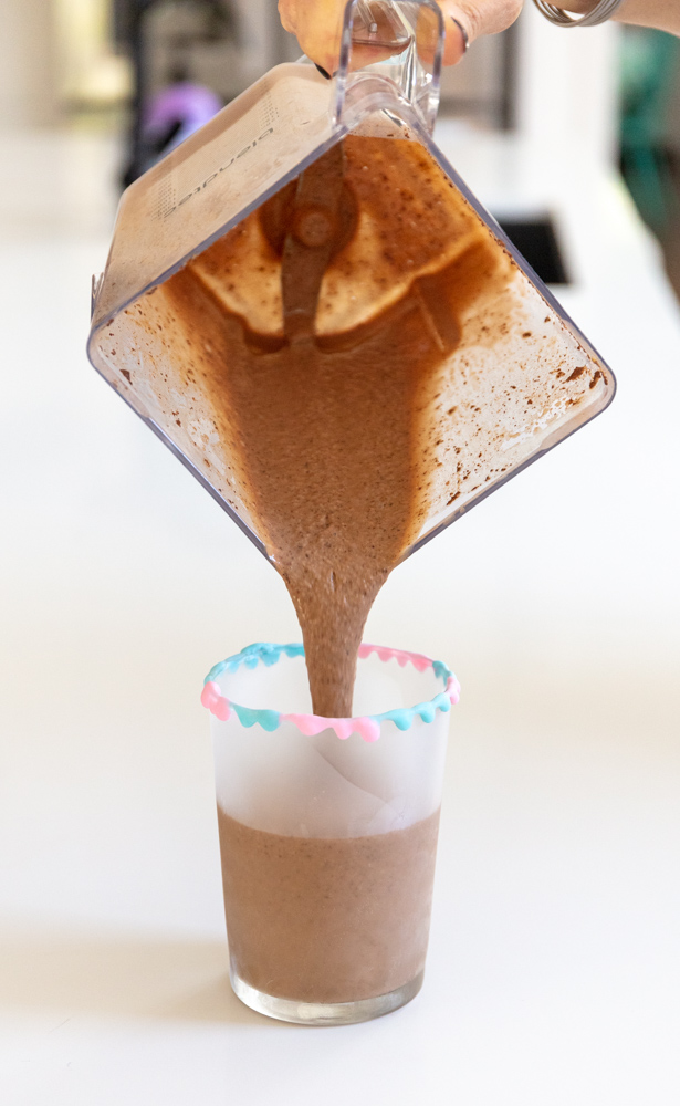 pouring vegan chocolate shake into a tall glass