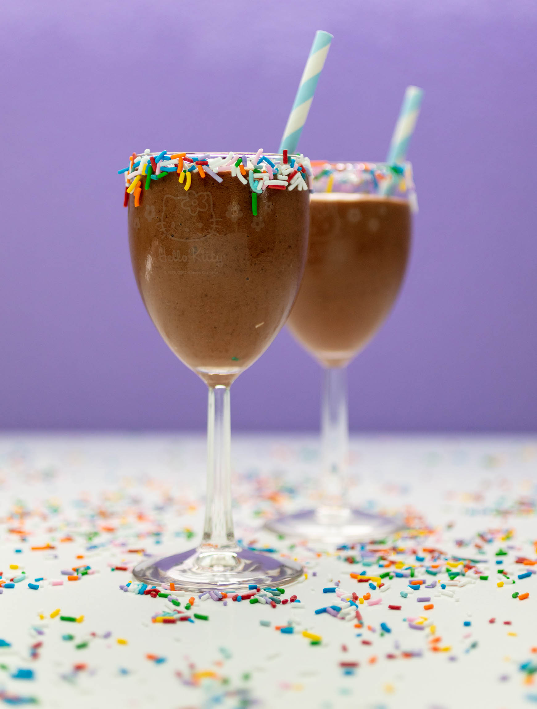 2 hello kitty wine glasses with sprinkles on the rim, filled with vegan chocolate shakes