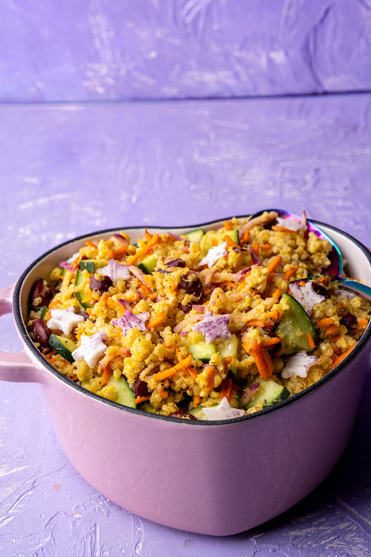 a pink heart-shaped dutch oven filled with a colorful millet, quinoa, and veggie salad