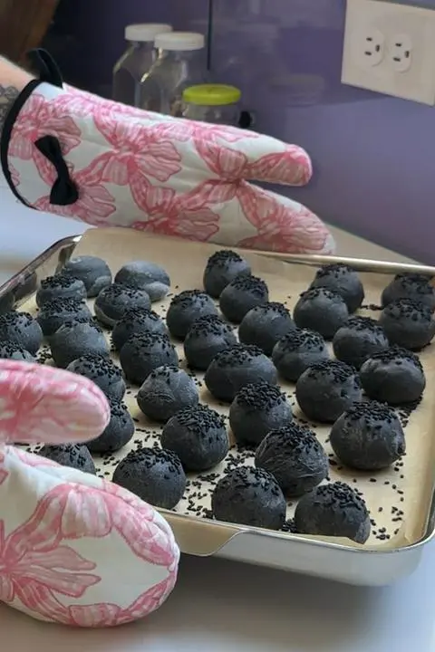 a tray of 38 baked black baby burger buns with black sesame seeds on top.