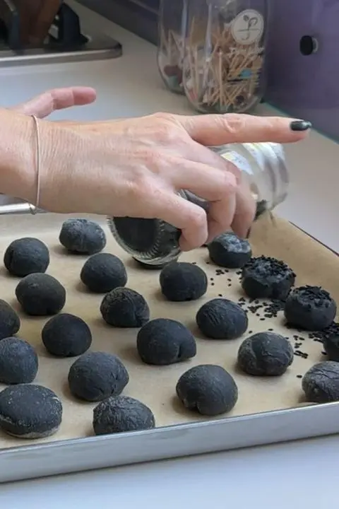 sprinkling black sesame seeds onto mini black buns.