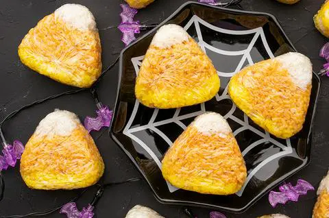 3 tuna onigiri that look like candy corn are on a black spider web plate, and there are purple bat lights around it and more vegan onigiri.