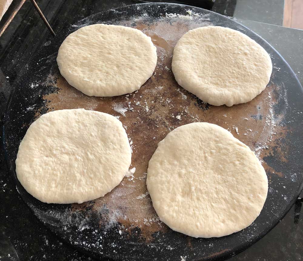 4 small round circles of vegan pizza dough on a baking stone