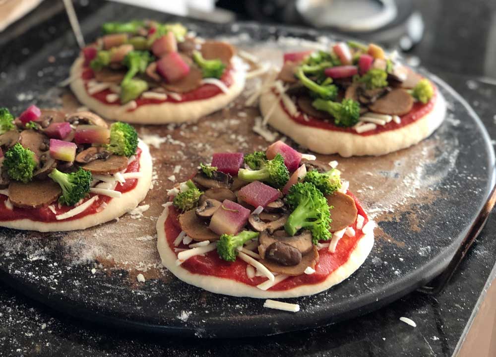 4 small round vegan pizzas on a baking stone and ready to bake