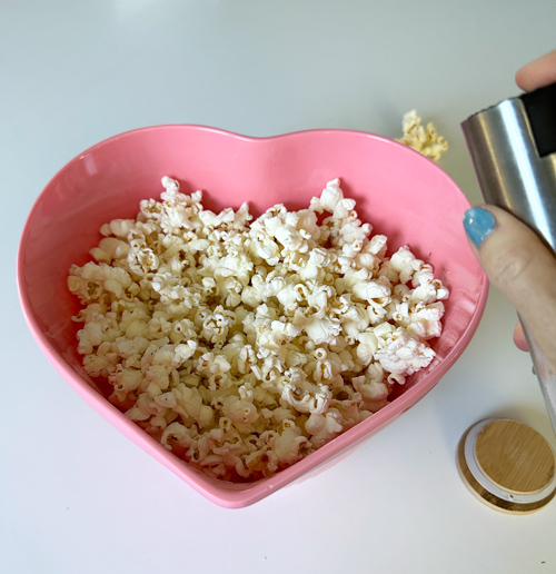 using an oil sprayer to spray the popcorn with olive oil