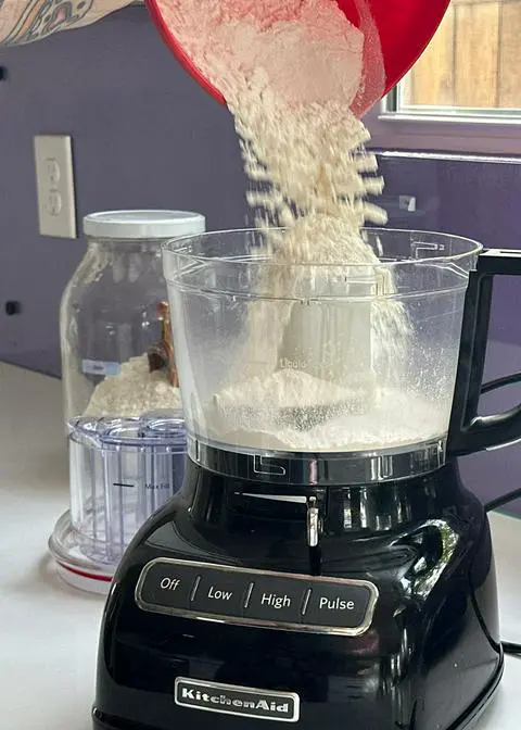 adding flour and vegan powdered sugar to a food processor.