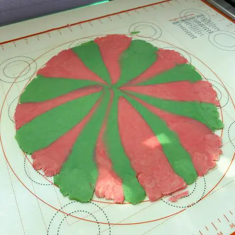 pink and green dough rolled thinly on a rolling mat.