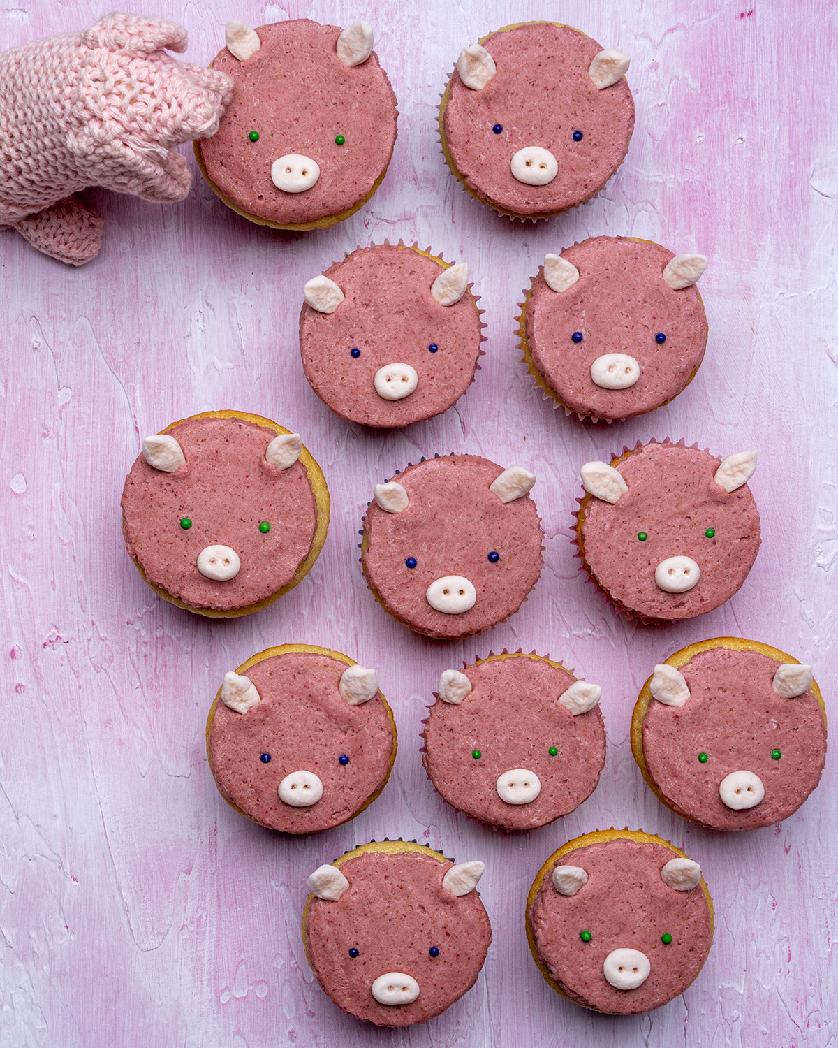 12 pig cupcakes with a small crocheted pig looking interested in one of them.