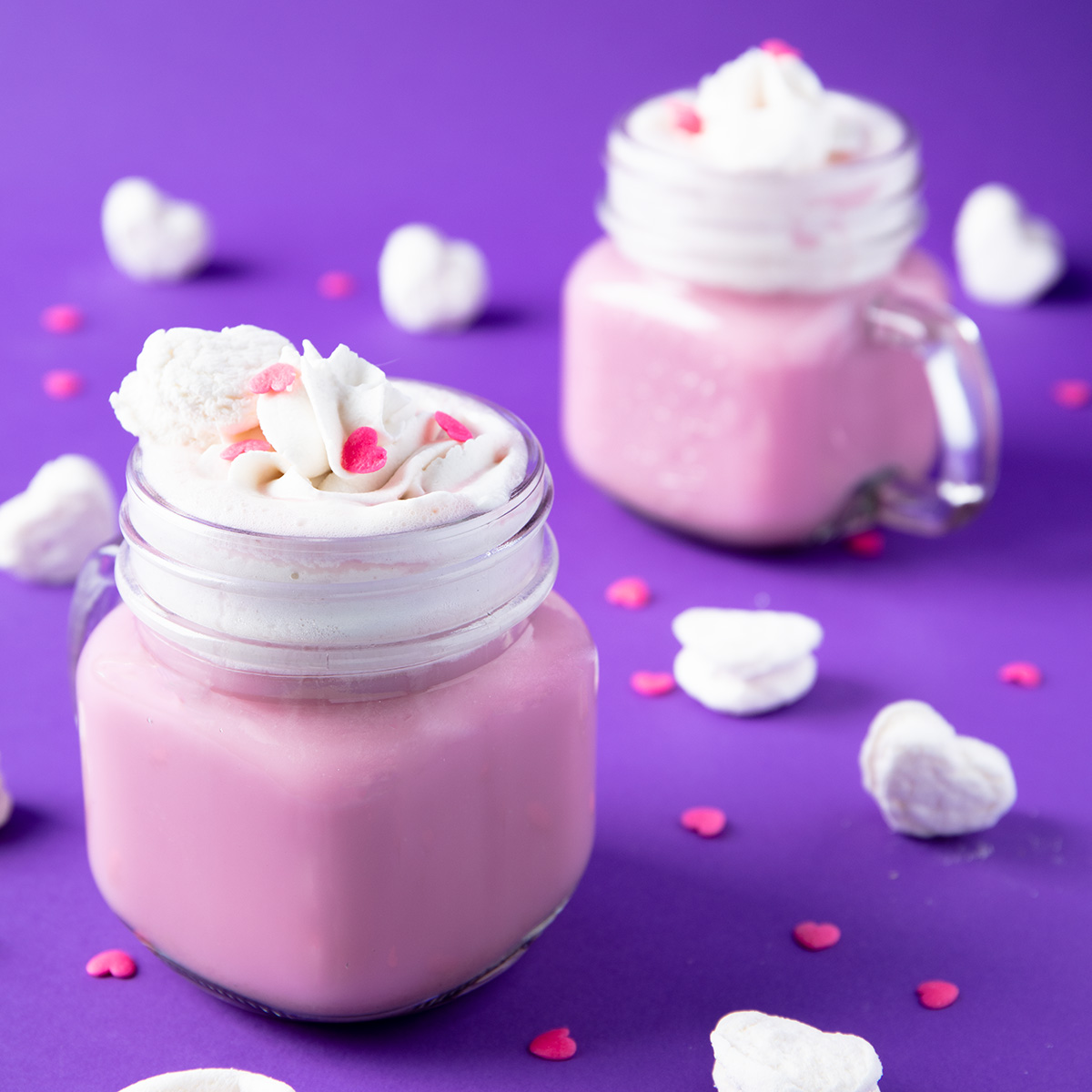 vegan pink peppermint hot cocoa in 2 cups with whipped cream, pink heart sprinkles, and heart shaped marshmallows