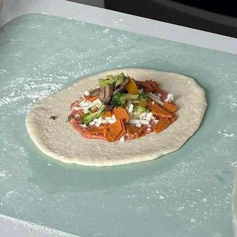 a round piece of pizza dough with a pile of vegan toppings in the center.